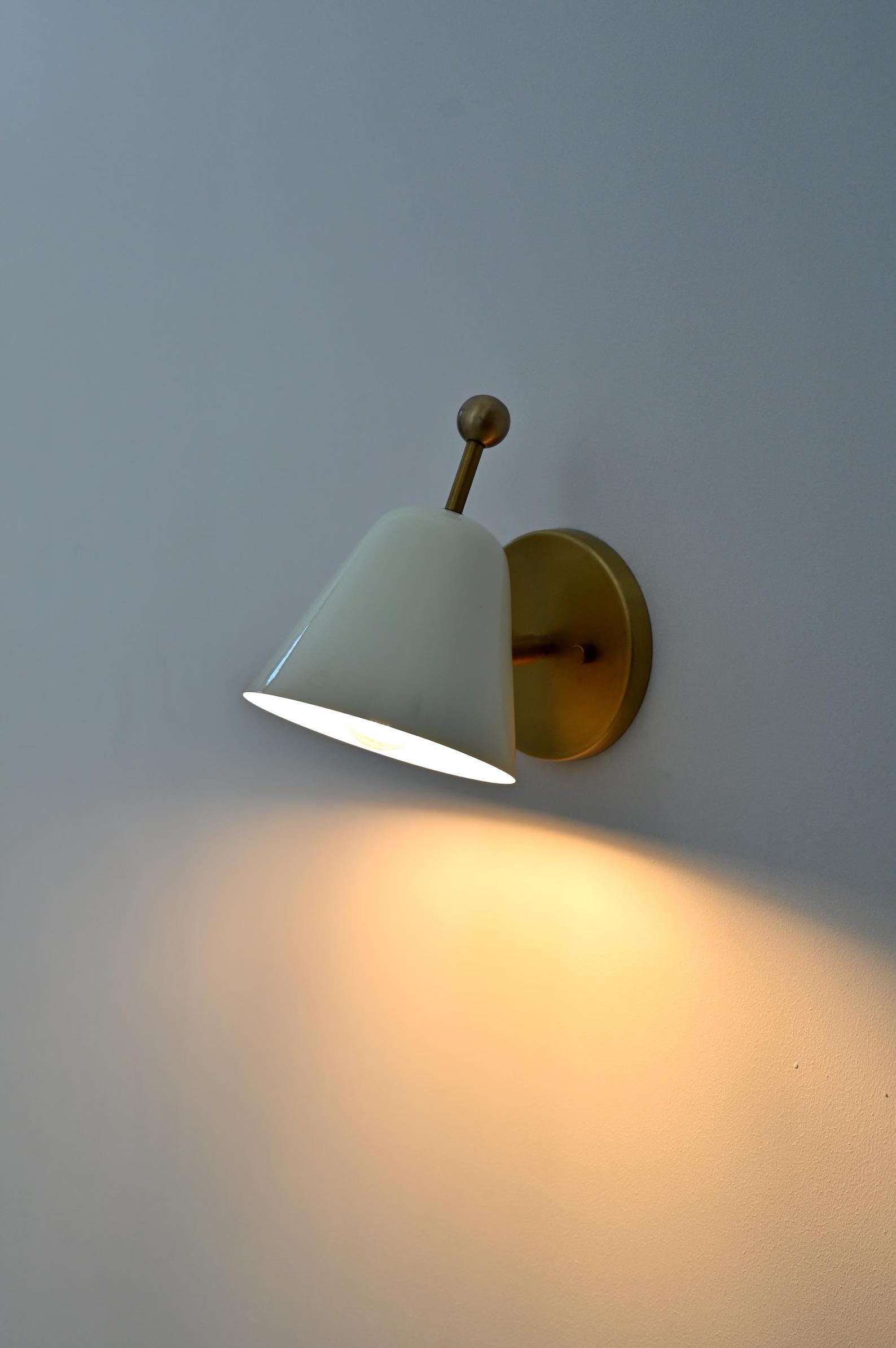 Ivory and brass wall sconce with cone shade, minimalist Nordic light fixture mounted on white wall.